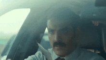a man with a mustache is driving a car with his seat belt on .