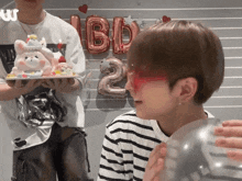 a man wearing red glasses is blowing up a balloon in front of balloons with the number 2 on them