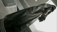 a person wearing a long black coat and gloves with a cross on the wrist