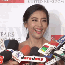 a woman stands in front of a bunch of microphones including one that says daradaily
