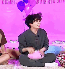 a man is sitting on the floor with his legs crossed holding a pink pillow