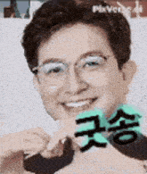 a man wearing glasses is smiling and holding a green heart shaped object .