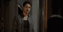 a man in a denim shirt is standing in front of a mirror .