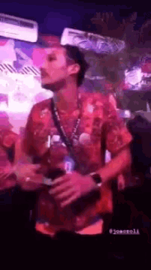 a man in a red shirt is standing in a dark room holding a drink .