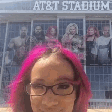 a woman with pink hair and glasses is taking a selfie in front of a sign that says at & t stadium .
