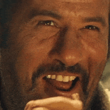 a close up of a man 's face with a beard covering his mouth with his hand .
