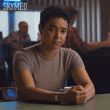 a woman sits at a table with a cup of coffee in front of a skymed sign