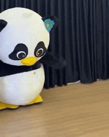 a stuffed panda with a yellow beak is standing on a wooden floor .