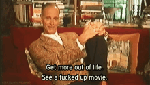 a man is sitting on a couch with his legs crossed and saying get more out of life see a fucked up movie