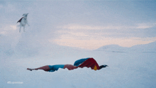 a man in a superman costume is flying through the air in the snow
