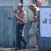 a shirtless man in adidas sweatpants stands in front of a wooden fence with the number 23 on it