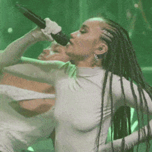 a woman with braids is singing into a microphone in front of a green background