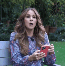 a woman is sitting on a bench holding a red cell phone in her hands .