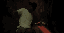 a man in a white shirt is sitting in a dark room with a bottle of beer