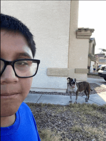 a boy wearing glasses stands in front of a dog