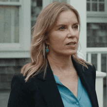 a woman wearing a blue shirt and a black jacket stands in front of a building