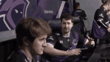 a man in a purple shirt is sitting in front of a team rival sign