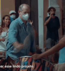 a man wearing a mask is playing a drum in front of a group of people