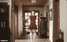 a woman in a red dress and white boots is standing in a hallway with the words wheeluv below her