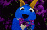 a blue stuffed animal smelling purple flowers
