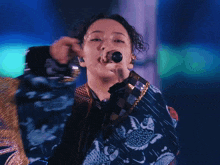 a woman singing into a microphone wearing a blue and gold jacket