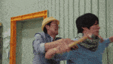 a man in a yellow hat is holding a hammer to another man 's neck