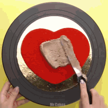 a person is spreading frosting on a heart shaped cake on a black plate that says mr.cakes