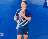 a man in a blue shirt is holding a tennis racquet in front of a blue wall with numbers 5 15 3 15 on it