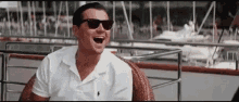 a man wearing sunglasses and a white shirt is sitting in a chair and laughing .