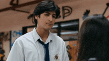 a boy in a white shirt and tie is talking to a girl in a classroom .