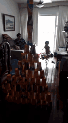 a woman sits on a couch in a living room while a boy plays with a tower made of cups