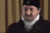 a man with a beard and a black hat with a cross on it .