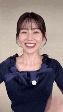 a woman wearing a blue shirt with ruffles and a white button on the front smiles