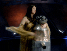 a woman in a gold dress is holding a robot in her arms