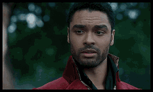 a man with a beard is wearing a red coat and a black shirt and says huh