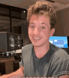 a man in a grey shirt is smiling in front of a speaker