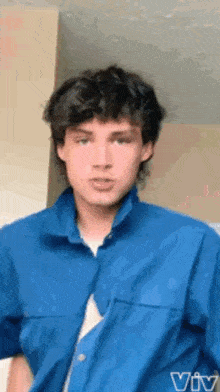 a young man in a blue shirt is standing in front of a wall .