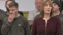 a woman in a maroon sweater with the letter m on it stands in a crowd