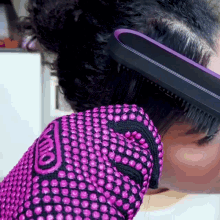 a woman wearing a pink glove is brushing her hair with a comb