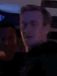 a man is making a funny face in a dark room with a purple light behind him .