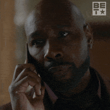 a man with a beard is talking on a cell phone with a be t logo in the background