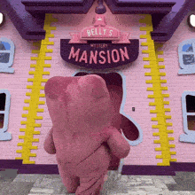 a pink teddy bear is standing in front of belly 's mystery mansion sign