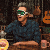 a man wearing ski goggles sits at a table next to a mug that says good mythical morning on it
