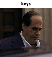 a man in a suit and white shirt is looking down with the word keys above him