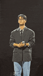 a man with glasses and a black jacket holds a microphone