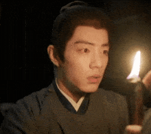 a man in a kimono is holding a lit candle in his hand .