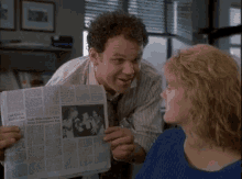 a man is holding a newspaper in front of a woman and pointing at it .