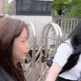 two girls standing next to each other in front of a metal gate