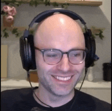 a bald man wearing headphones and glasses is smiling and looking at the camera .