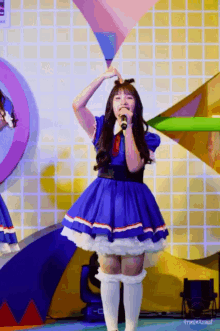 a girl in a blue dress is singing into a microphone on a stage